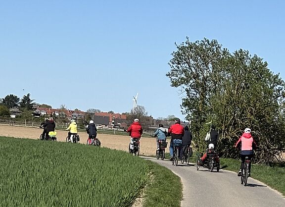 Merherer Radler von hinten auf einem Feldweg im Fruehling bei blauem Himmel